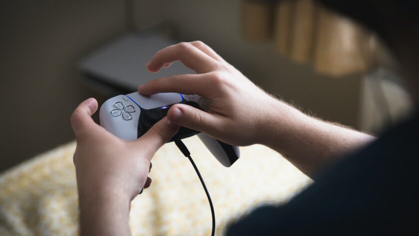 Boy holding a PlayStation 5 video game controller and using the joypad to play games indoors